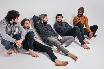 Relaxed Men Of Diverse Appearance Sit On Floor After Shooting, Have Talk, Wearing Casual Fashionable CLothes Outfit. People and fashion concept