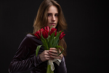 Studio portrait of a young woman on black background with a bouquet of red tulips in her hands