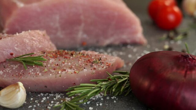 Close up of fresh pork is sprinkled with pepper, spices and seasonings on background of onion, garlic and greens. Food concept, cooking meat, loin, carbonate.