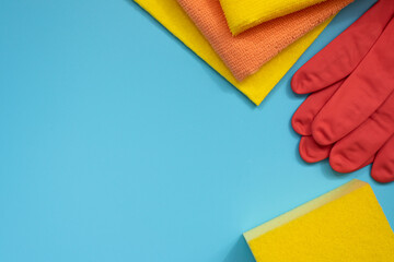 House cleaning supplies: sponge, rubber gloves and cloths on blue background. Top view. Copy space.
