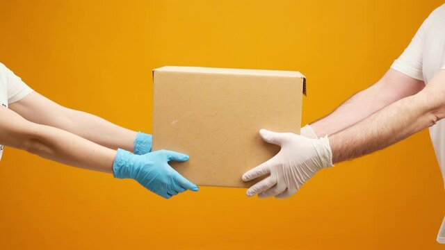 Human hands in gloves passing Donation box to the other one against yellow background, Coronavirus donations help