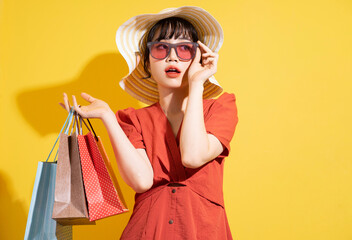 Young Asian businesswoman holding shopping bags posing on yellow background