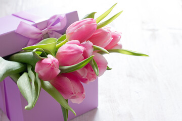 Decorative gift box with purple ribbon and tulips inside on light background