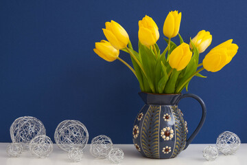 jug with large yellow tulips and metal decorative balls, on a blue background