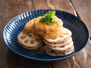 蓮根料理。蓮根でミンチ肉を挟んでこんがり焼いた料理に大葉とソースをトッピング。