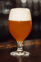 A glass of beer on the table in a dark bar. Background bokeh.