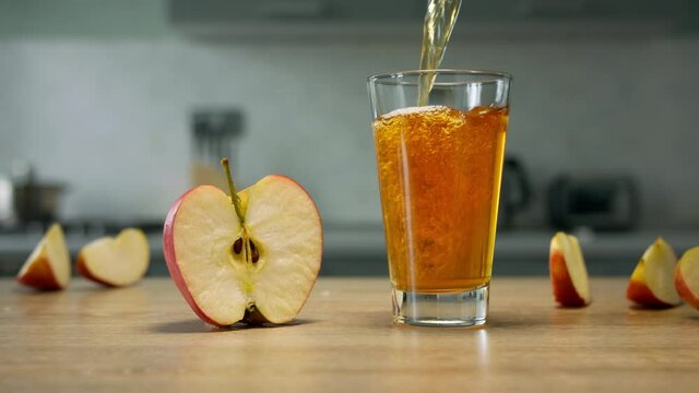 Filling glass with apple juice with apple slices on background. Close up 