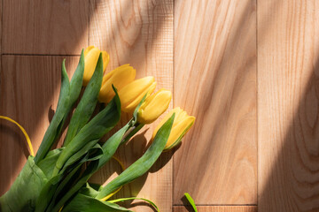 Beautiful yellow tulips on a wooden textured background, on a parquet. A bouquet of yellow flowers with green leaves on parquet boards in the rays of the spring sun. Spring yellow-green bouquet.