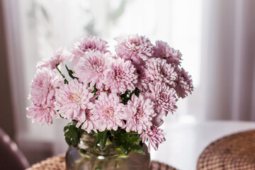 A bouquet of gray chrysanthemums stands on the table in a gray glass vase on a light background