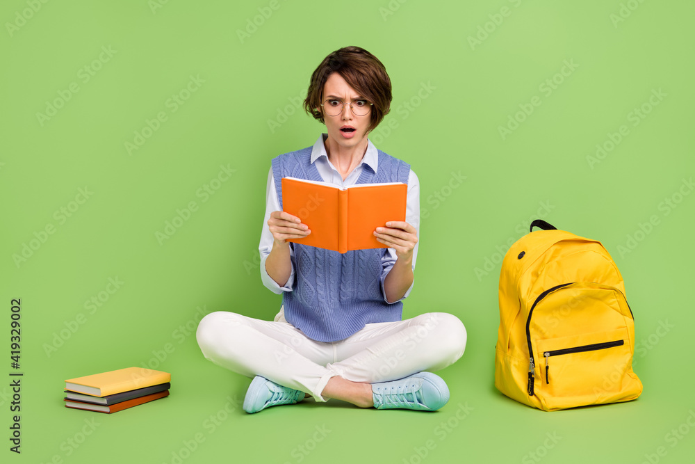 Poster Portrait of attractive worried girl sitting lotus position reading book diary bad mark isolated over green color background