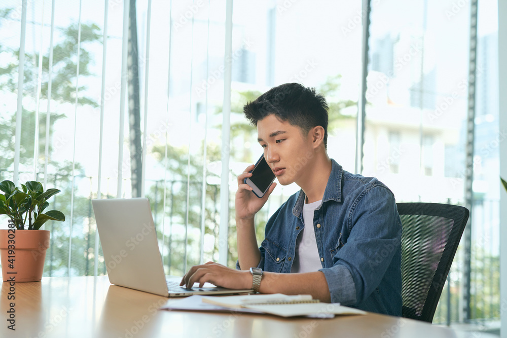 Poster smiling man writing notes while making phone call and using laptop at home