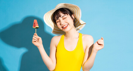 Beautiful Asian woman wearing yellow jumpsuit on blue background and eating tropical fruits, summer concept © Timeimage