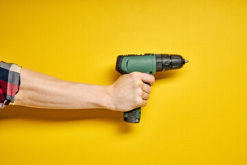 Green cordless battery powered drill on yellow background, cropped male hands holding tool for...