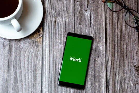 02/10/2021 Portsmouth, Hampshire, UK A mobile phone or cell phone laid on a wooden table with the iHerb app open on screen next to a coffee