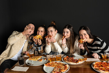 4 girls and a boy bite into a piece of pizza having fun.