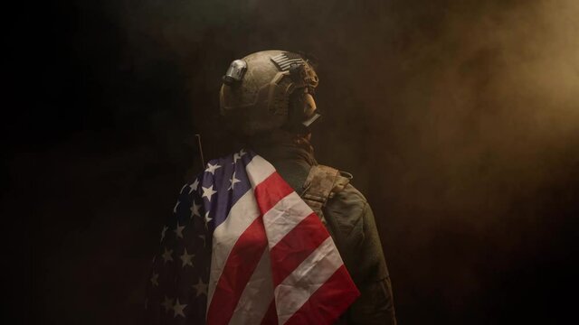Special forces soldier standing with his back to us in the dark holding USA national flag