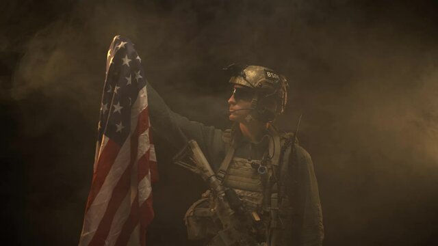 Special forces soldier standing in the dark and raising up USA national flag