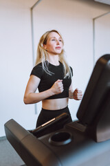 Fototapeta na wymiar Attractive young blonde woman run on treadmill in fitness sport club. Fitness, cardio, weight loss