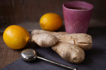 Ceramic mug of hot tea with tea strainer, ginger root and lemons on the table. Organic Alternative Therapy Concept.