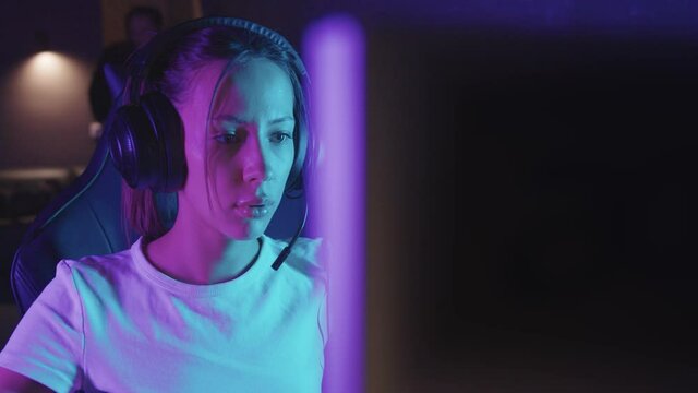 Young concentrated gamer woman sits at the computer in the gaming club and playing the game