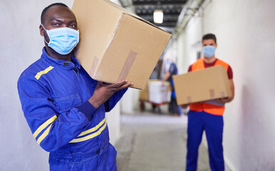 Zwei Arbeiter mit Mundschutz tragen Kartons