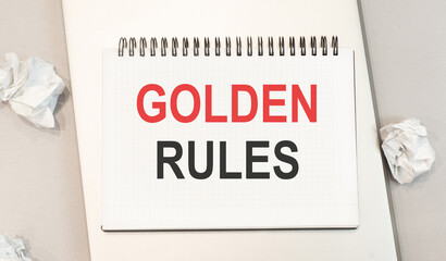 The word golden rules is written in a notebook that sits on a gray desktop along with a laptop. Business image