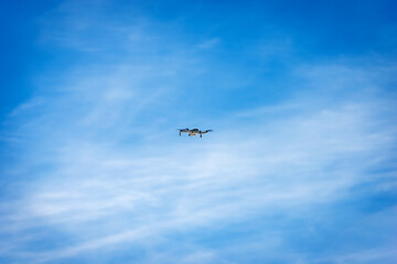 Fototapeta na wymiar Small white drone flying on blue sky with clouds and copy space, photography.
