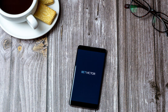 02-24-2021 Portsmouth, Hampshire, UK A mobile phone or cell phone on a wooden table with the Bet Victor app open next to a coffee and glasses