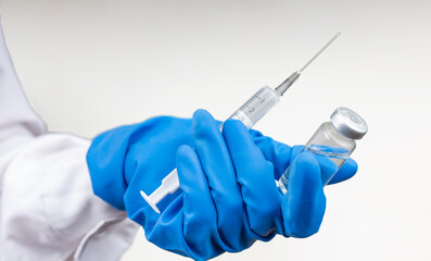 Vial withCOVID-19 vaccine and a syringe with a needle for injections for coronavirus infection in the hand of a doctor in a nitrile glove on a white background. Close-up. Concept fighting Coronavirus