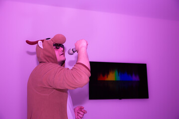 Man in cosplay costume of a cow singing karaoke. Guy in the funny animal pyjamas sleepwear holding...
