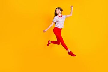 Photo of funky lady jump raise arm run wear striped shirt red trousers footwear isolated yellow color background
