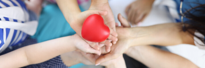 Hands of adults and children hold red heart in middle. Love and health in families concept