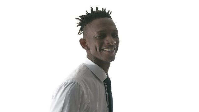 Young black man stands in profile on a white background and turns smiling. A black man in an office suit smiles and looks into the camera.