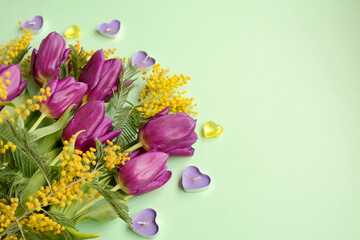 Beautiful arrangement of spring flowers. Lilac tulips and mimosa branches on a background of mint....