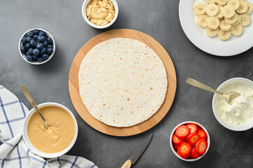 Tortilla cooking process with different fillings of peanut butter, banana, strawberry, blueberry, almond. Food trend. Sweet sandwich for breakfast. Trendy way of wrapping. Top view, copy space