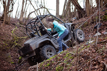 A girl is standing by an SUV that has moved into a ditch. Winch coupled to ATV that drove off after extreme riding © lexashka