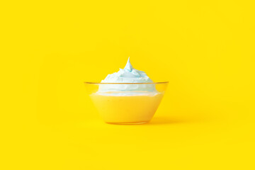 beaten eggs with sugar in a glass plate, over yellow background, culinary concept