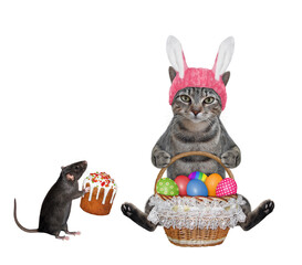 A gray cat in a pink easter bunny hat is holding a wicker basket of colored easter eggs. White...