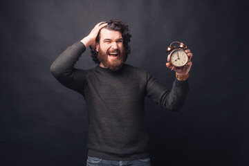 Photo of afraid handsome man looking at alarm clock over black background