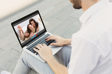 Remote communication concept. Young guy using laptop computer to talk to his wife and daughter online, outdoors