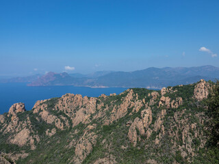 Fototapeta premium Aerial video from Calanques de Piana. Corsica red rocks located in Piana, between Ajaccio and Calvi. Over the Mountains range we see the Golf of Porto. Tourism and vacations concept.