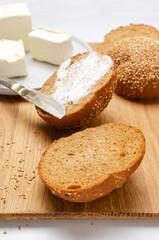 Vertical image.Fresh and tasty rye bun with sesame, creamy butter on the plate, knife on the wooden board