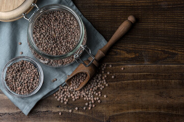 Tarro de cristal con lentejas crudas junto a un pequeño bol de cristal y una cuchara de especias, todo ello sobre una mesa de madera oscura en que que queda espacio para texto, copyspace