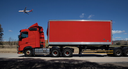 Truck on a freeway with plane flying overhead in Australian Country Town midway between Sydney and Melbourne with nice blue sky and lush green trees as a backdrop