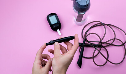 Person using lancelet on finger to check blood sugar level. Sport equipment and water on...