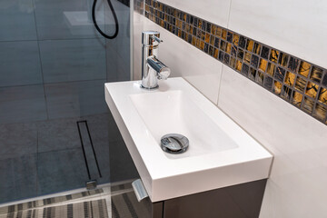 A small rectangular sink with a silver tap on the left in a tiled bathroom.