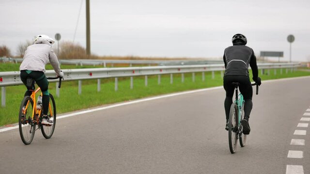 Two athletes are training on a bicycle. They are finishing their workout and one of them is riding and holding his hands up. Training in the cold season. Shooting from behind. 4K.