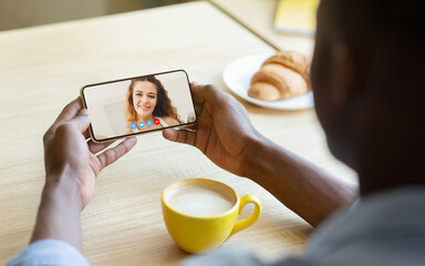 Young man having online video conference with his girlfriend on mobile phone while drinking coffee at cafe