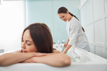 Female resting in tub while spa worker holding a hose