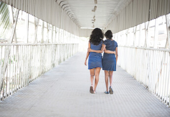 Two Indian asian girls walking on the street holding each other. Back view of teenage best girl friends.